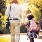 African American father and daughter running trough park.