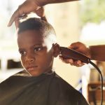 little boy getting his head shaved by barber with bored expression