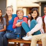 Group Of Children Sitting On Bench In Mall Smiling To Camera