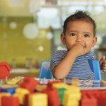 Happy baby playing with toy blocks in the kindergarten.