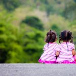 Rear view of two little girl sitting on ground at park